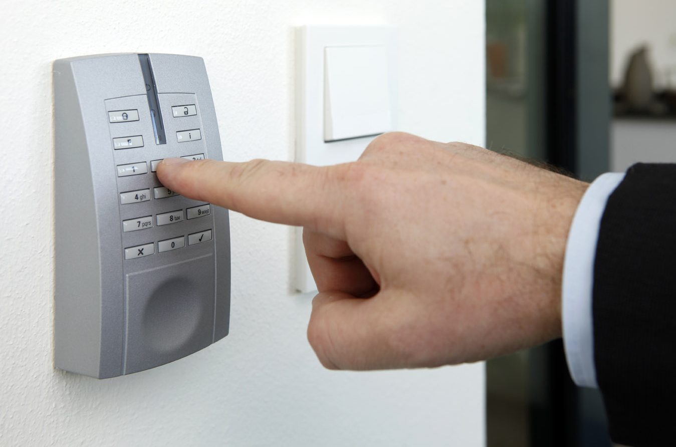 Hand drückt eine Taste auf einem an der Wand montierten Zugangskontrollgerät.